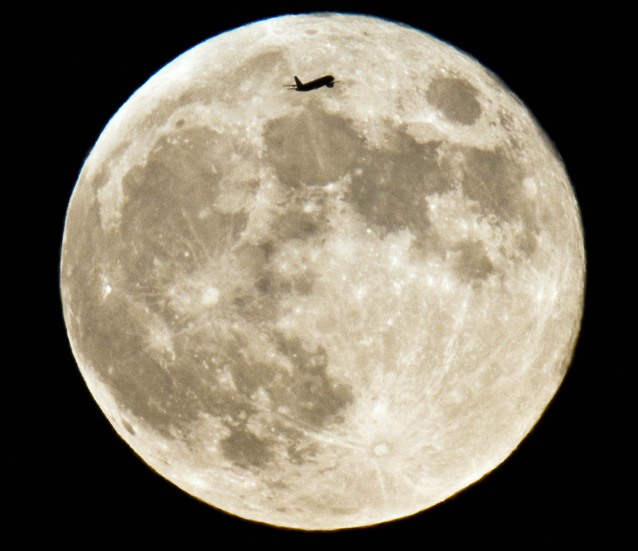 Ein Passagierflugzeug fliegt an einem Vollmond vorbei.